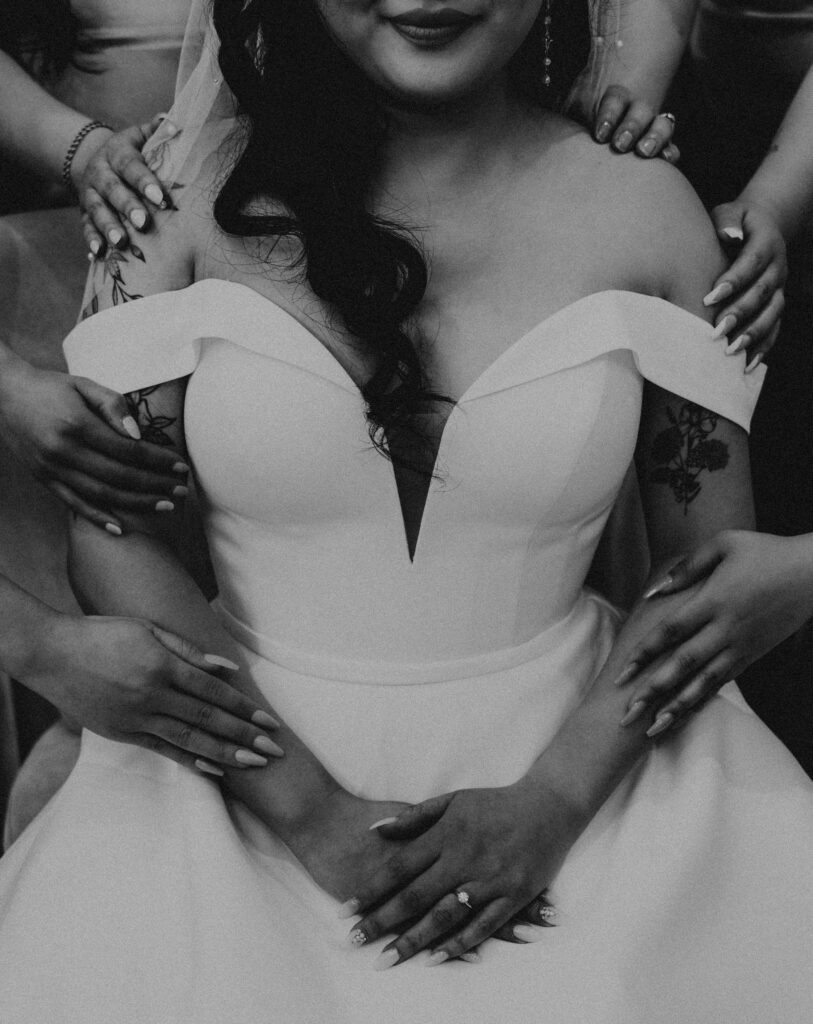 Bride and her bridesmaids touching her hands and shoulders to show support