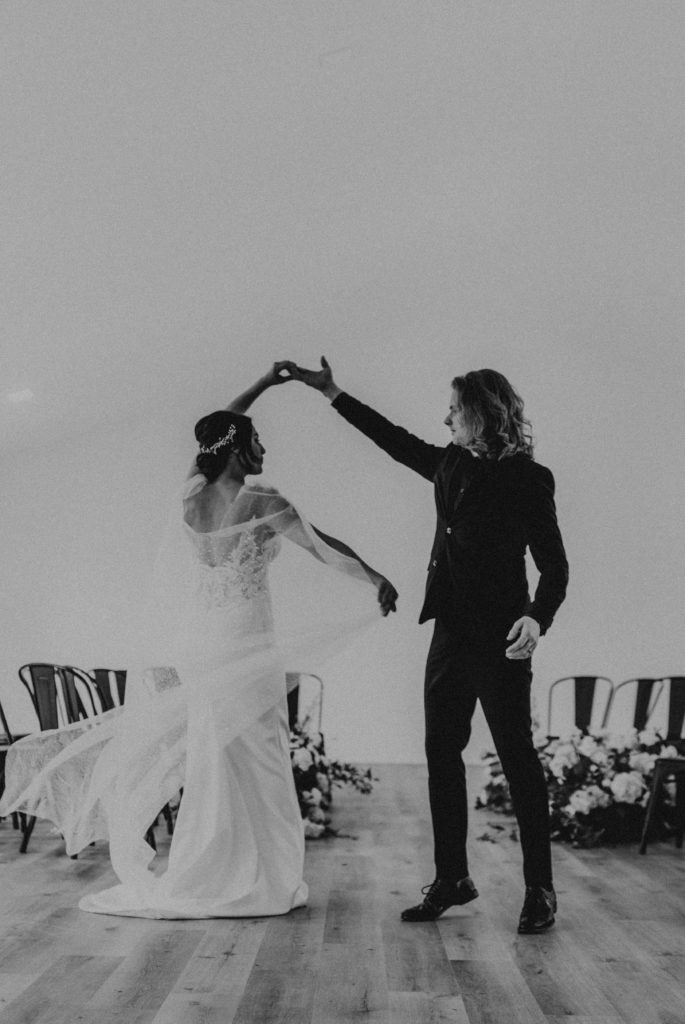 Candid black and white image of groom twirling the bride.